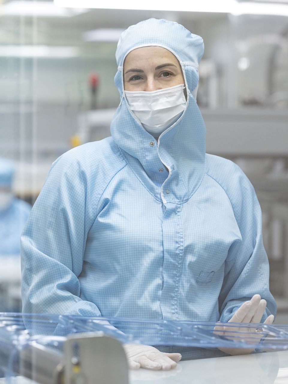 Eine Frau trägt in einem Reinraum einen Schutzanzug und eine Maske.