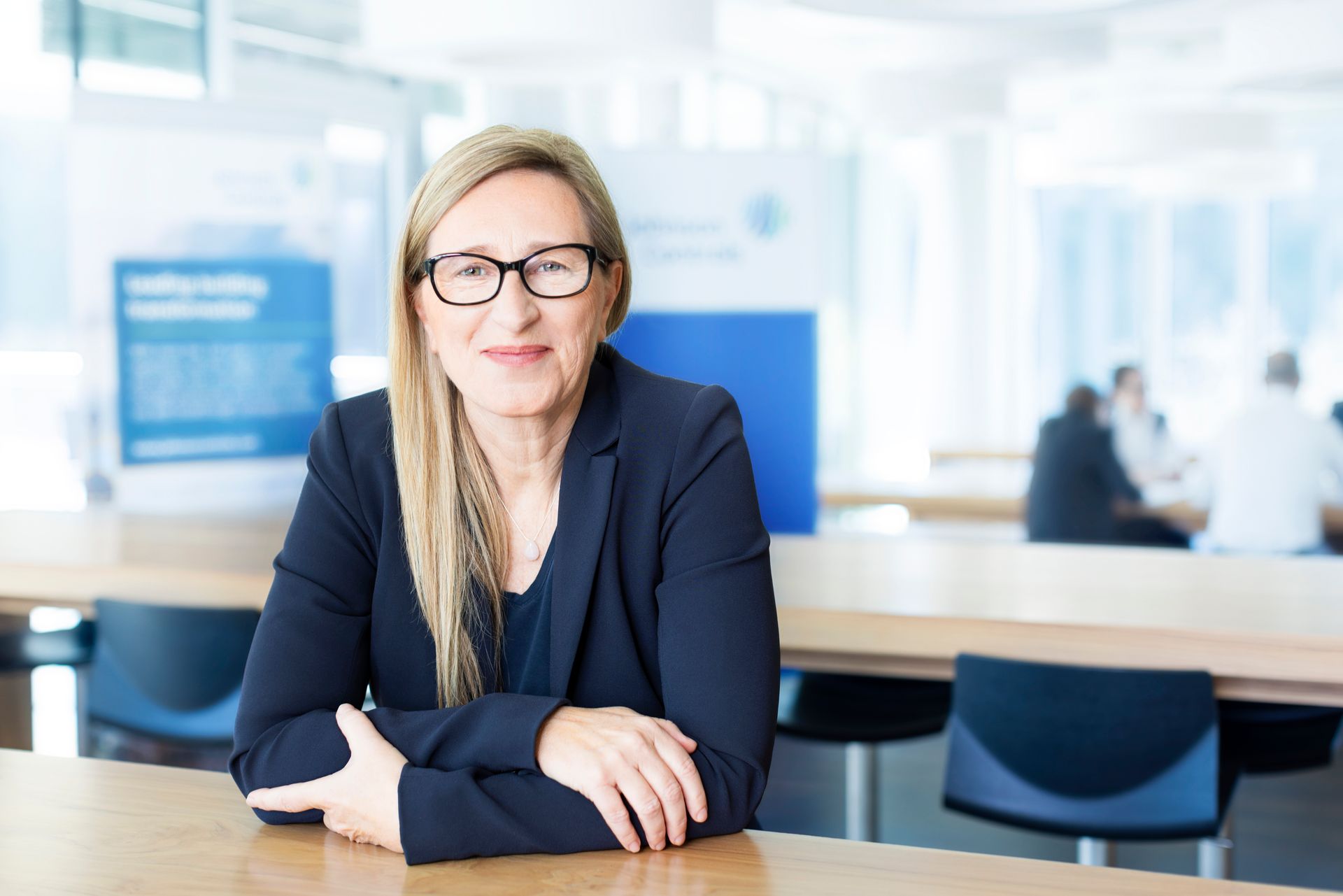 Eine Frau mit Brille sitzt mit verschränkten Armen an einem Tisch.
