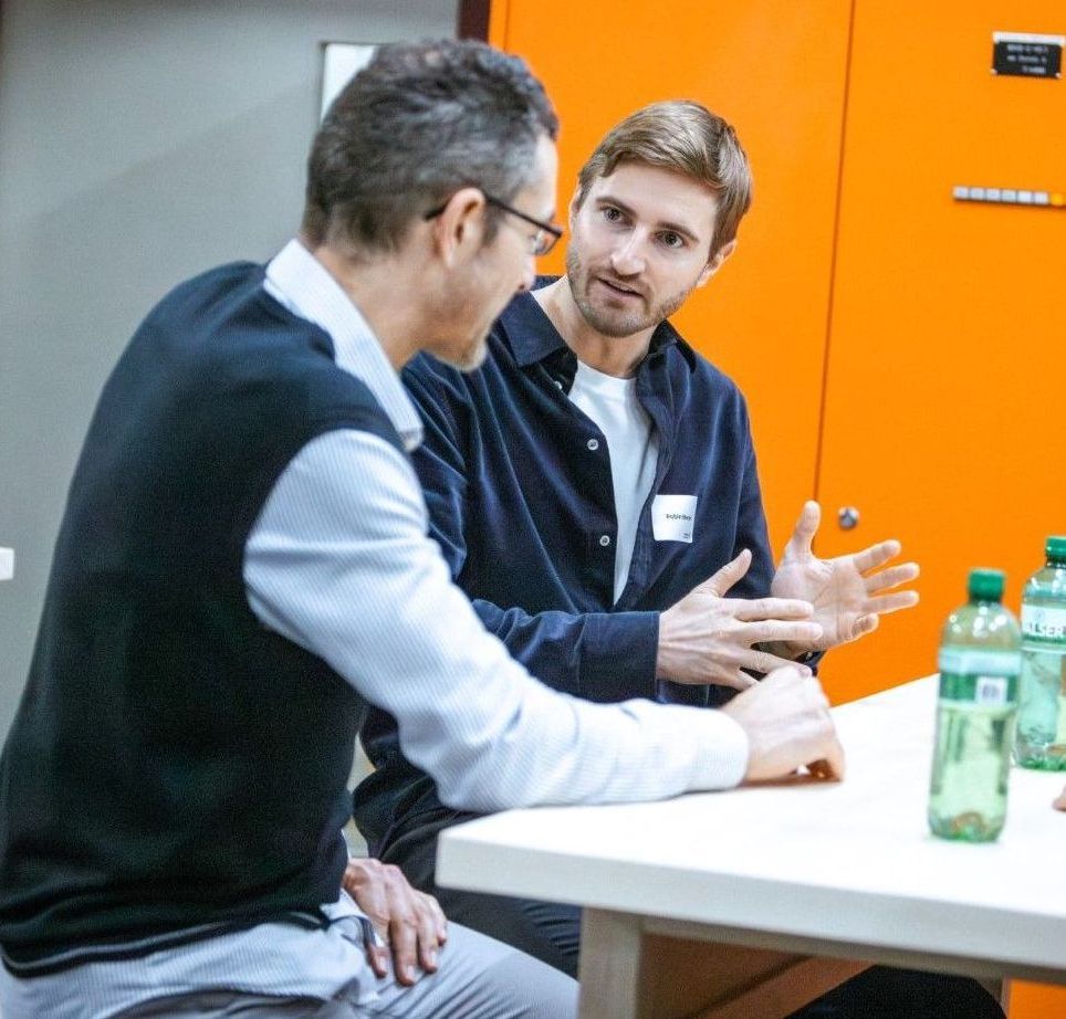Zwei Männer sitzen an einem Tisch und unterhalten sich.