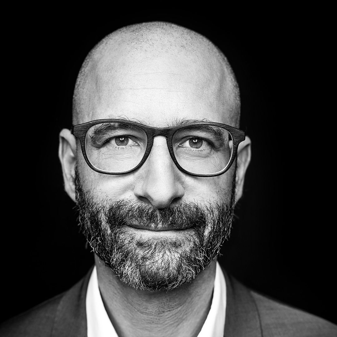Auf einem Schwarzweissfoto lächelt ein kahlköpfiger Mann mit Bart und Brille.