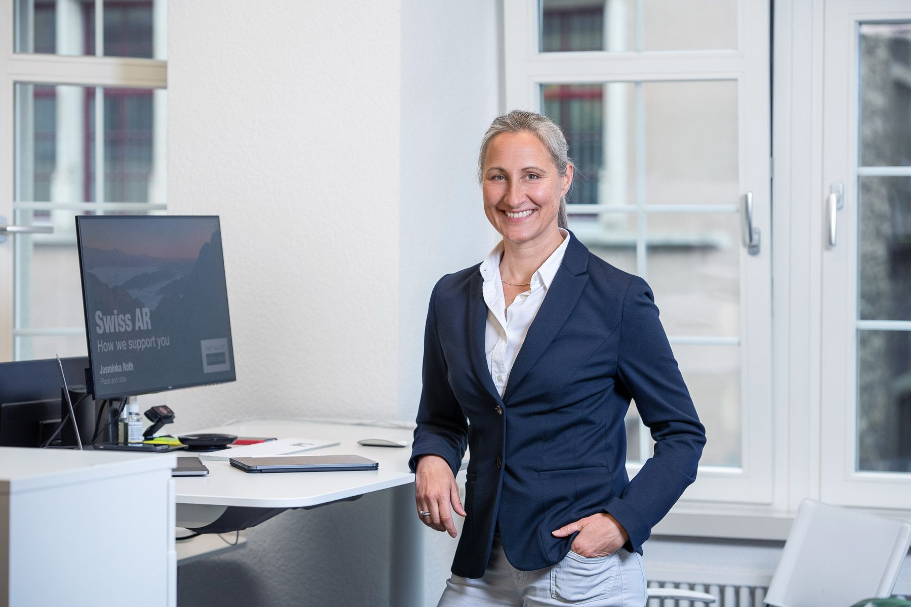 A woman is standing in front of a desk with a computer.
